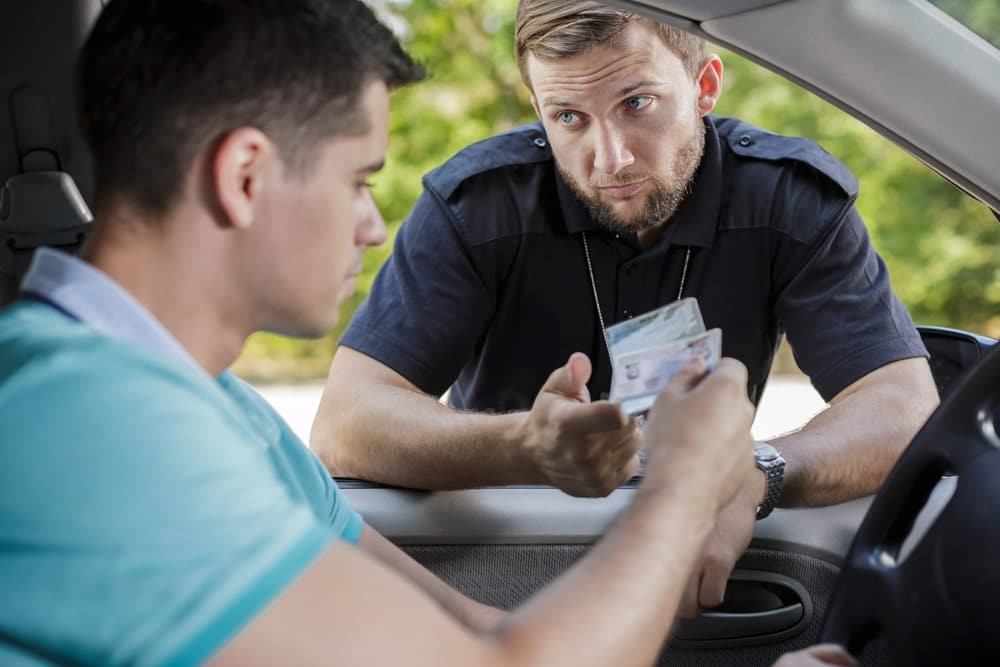 Image shows a police officer examining a driver’s license during a traffic stop, concept of how a license suspension after a UT DUI can begin.