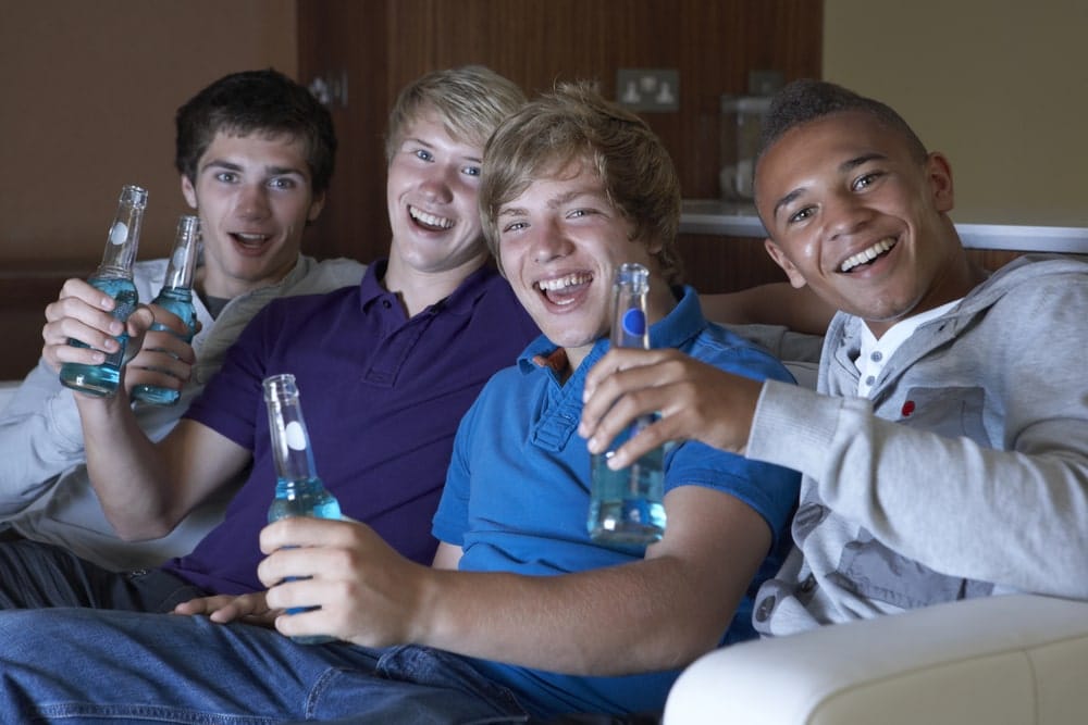Image is of a group of young men holding bottled drinks inside a dorm style setting, showing behavior that may lead to alcohol violations in UT dorms.