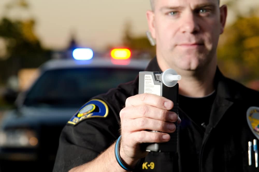 Image shows a police officer holding a breathalyzer device during a traffic stop, demonstrating how officers test drivers suspected of impairment.