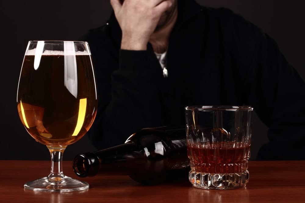 Image is of alcoholic drinks on a table with a distressed individual in the background, reflecting the emotional and legal impact of a DUI arrest at UT.