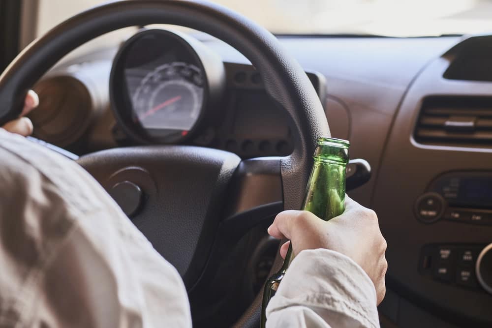 Image is of a person holding a beer bottle while seated in a car, representing risky behavior that can lead to a DUI arrest at UT and serious legal trouble.