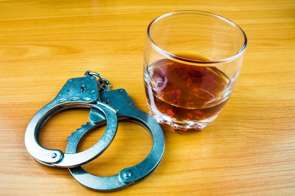 Image is of handcuffs placed beside a glass of alcohol, representing social hosting liability and potential legal consequences tied to UT parties and alcohol violations.