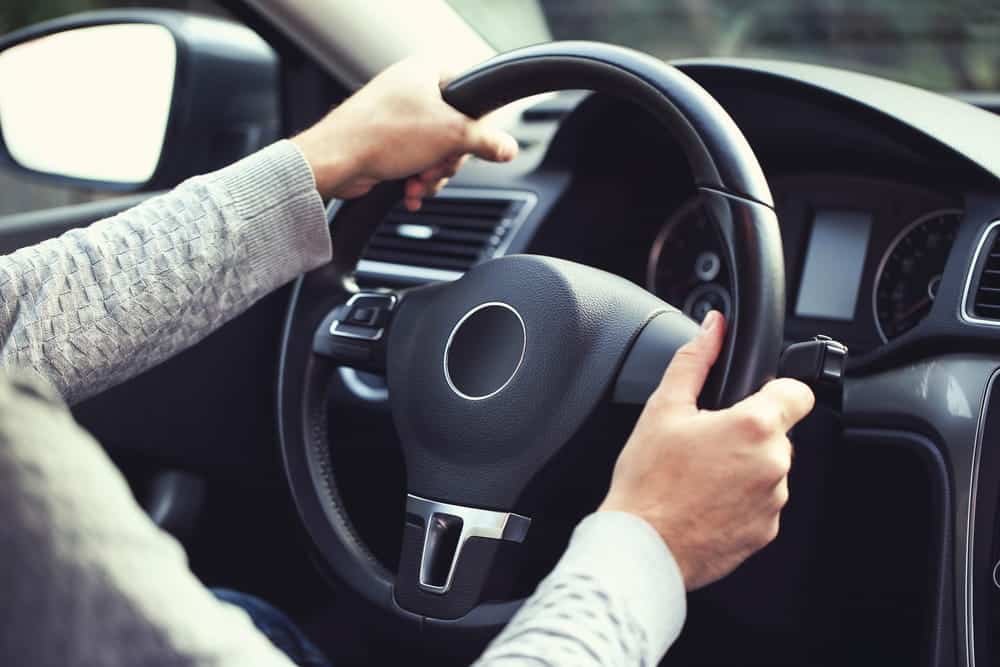 Image is of a driver holding a steering wheel inside a vehicle, representing decision making and legal consequences related to underage DUI.